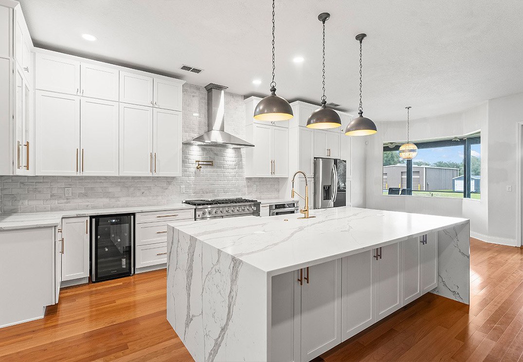 Bright white kitchen remodel with custom cabinetry, a quartz waterfall island, marble-look backsplash, hardwood floors, and pendant lighting